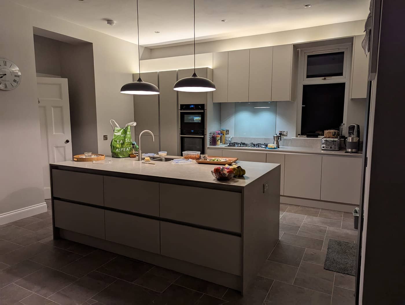 The completed kitchen with handleless units, an island and pendant lights, photographed in the evening