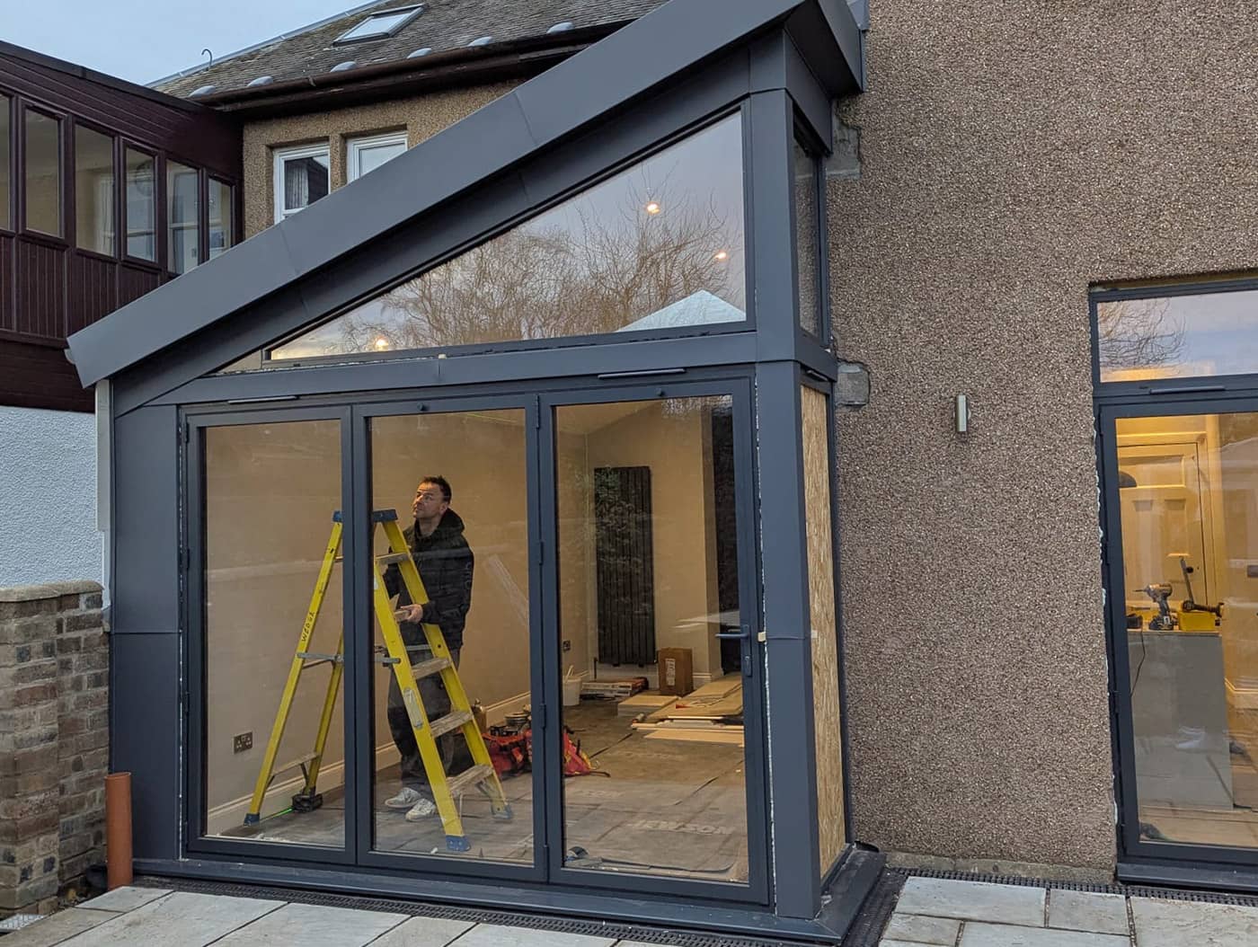 A glazed single-storey extension nearing completion, with a tradesperson on a stepladder inside